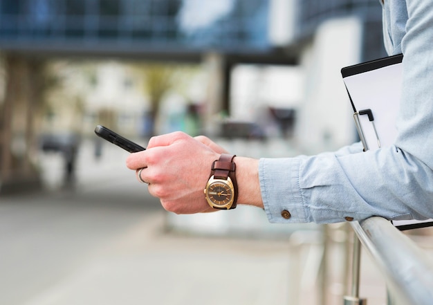 La mano dell&#39;uomo d&#39;affari con l&#39;orologio da polso elegante che per mezzo del telefono cellulare