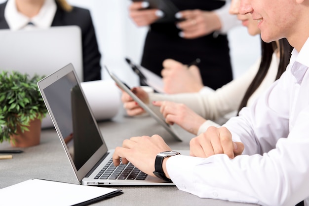 La mano dell&#39;uomo d&#39;affari sorridente facendo uso del computer portatile che si siede con il suo collega allo scrittorio