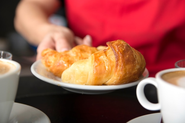 La mano della cameriera che offre il croissant al forno fresco in piatto