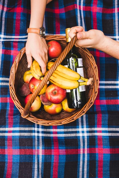 La mano della coppia sul cestino da picnic con frutta e bottiglia di champagne