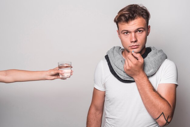 La mano della donna che dà bicchiere d&#39;acqua all&#39;uomo che prende le capsule su fondo grigio