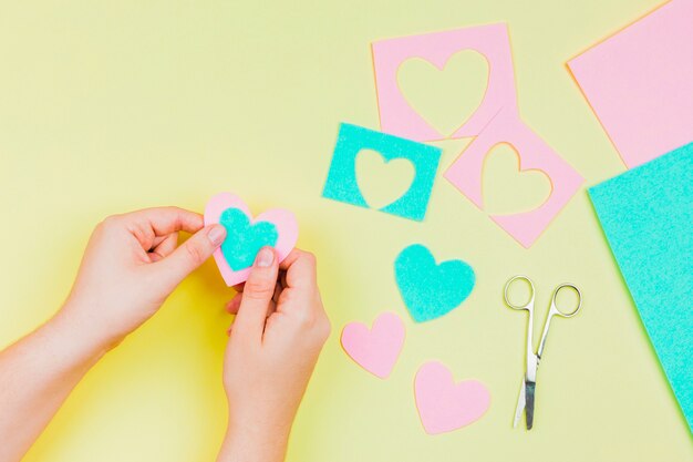 La mano della donna che fa a forma di cuore con carta blu e rosa su sfondo giallo