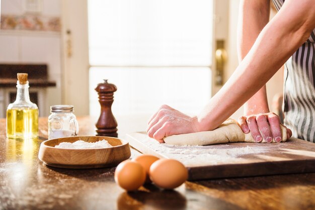 La mano della donna che impasta la pasta con gli ingredienti sulla tavola di legno