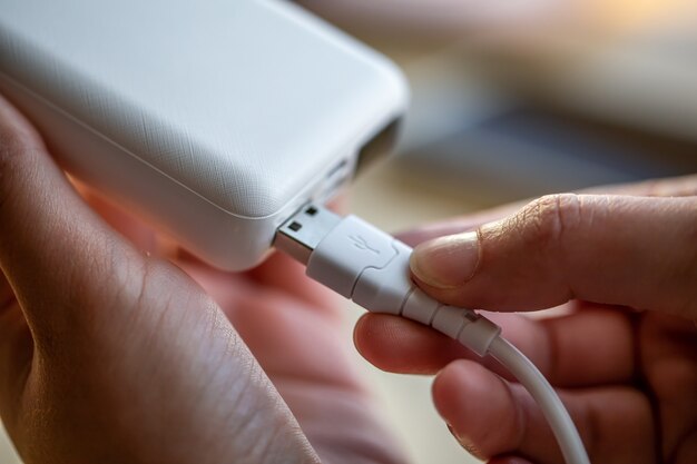 La mano della donna che tiene il cavo USB bianco e il power bank bianco