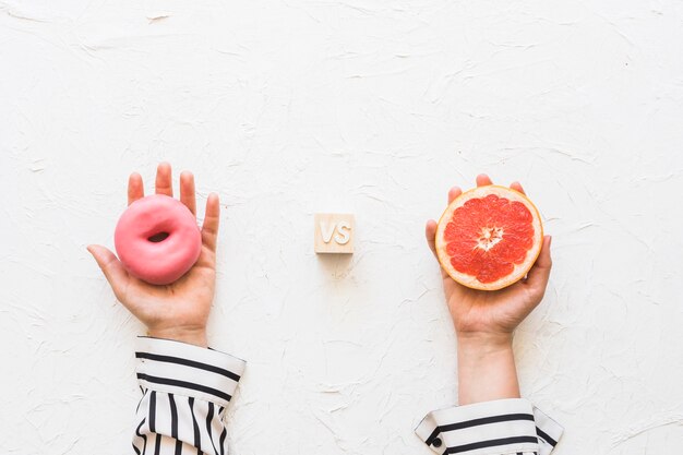 La mano della donna che tiene la ciambella rosa contro la fetta del pompelmo sopra il contesto strutturato