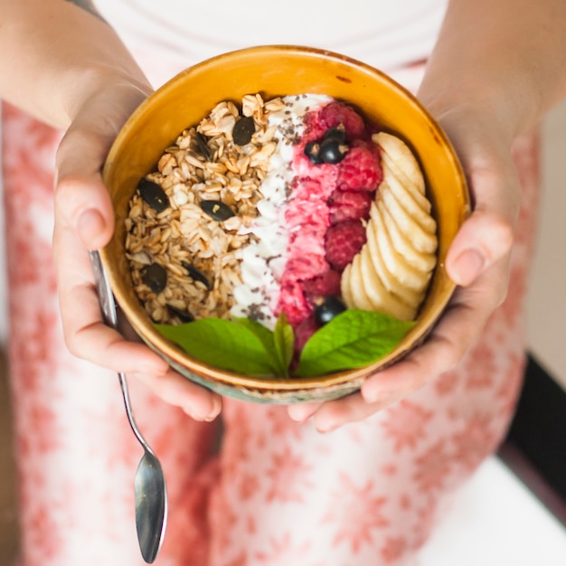 La mano della donna che tiene la farina d&#39;avena saporita con le bacche e le fette della banana in ciotola