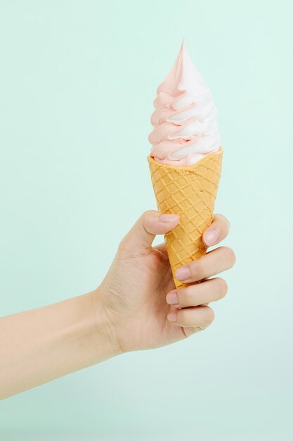 La mano della donna che tiene un delizioso gelato morbido in un cono di cialda croccante sulla superficie blu