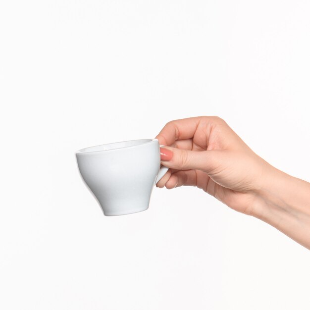 La mano della donna con la tazza sulla parete bianca