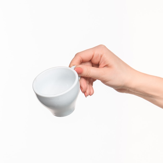 La mano della donna con la tazza sulla parete bianca