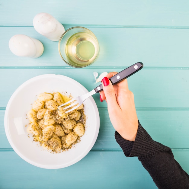 La mano della femmina che mangia la pasta di gnocchi con la forcella