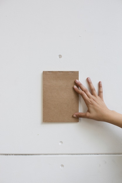 La mano della persona che tiene un blocco note marrone su una parete bianca