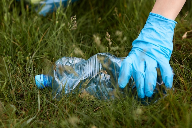 La mano della persona in guanto di lattice blu raccoglie la bottiglia di plastica da terra