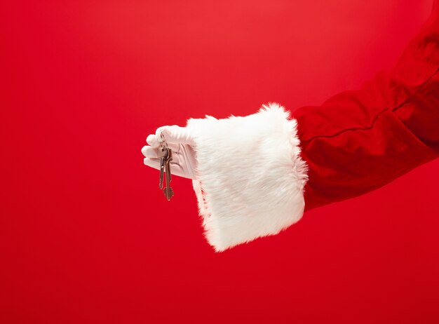 La mano di Babbo Natale che tiene un appartamento o le chiavi della macchina come regalo sul rosso