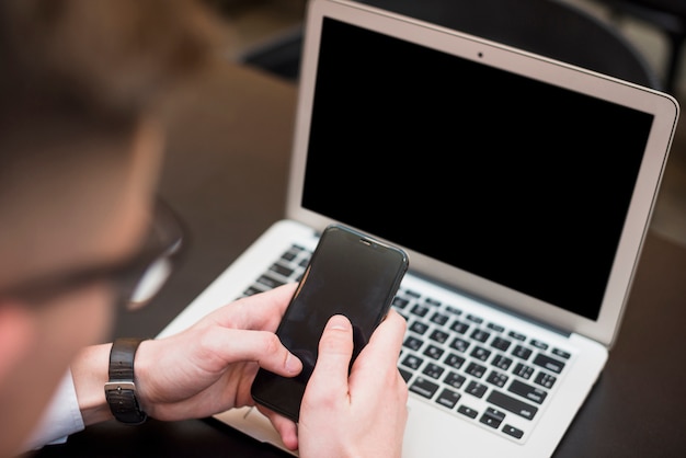 La mano di un uomo d&#39;affari utilizzando il telefono cellulare davanti al computer portatile