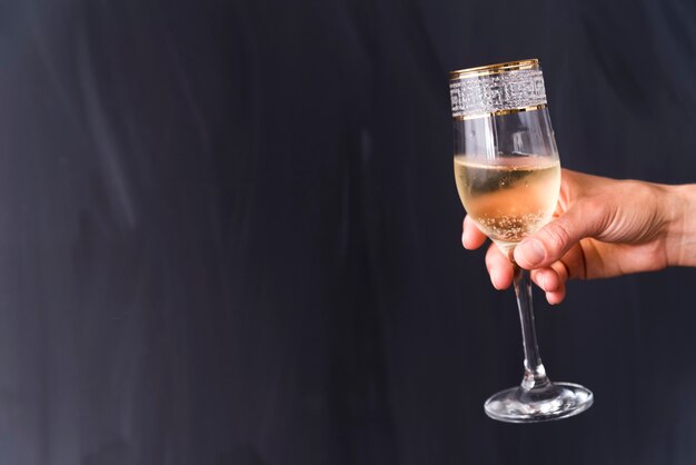 La mano di una persona che tiene il vetro elegante del champagne con la bolla contro il fondo nero