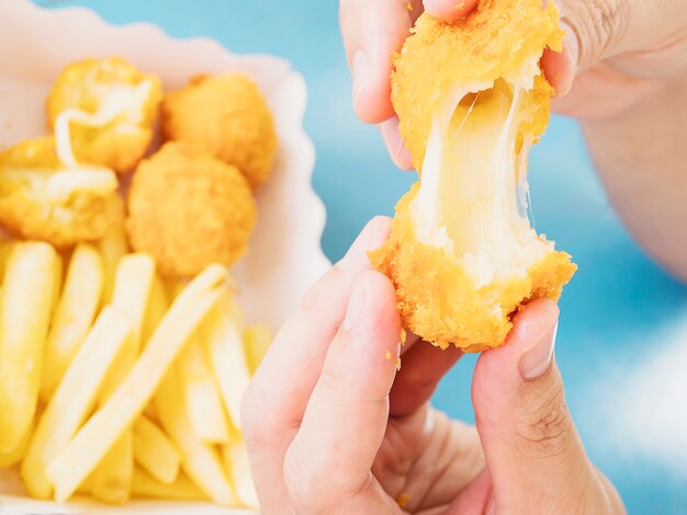 La mano è in possesso di una palla di formaggio stretch pronta per essere mangiata con patatine fritte morbide e concentrate