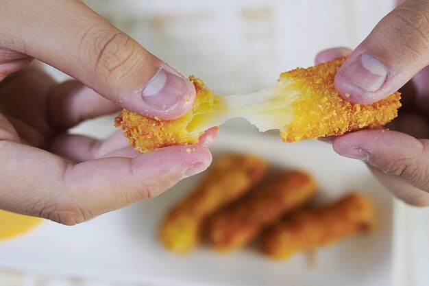 La mano è in possesso di una palla di formaggio stretch pronta per essere mangiata con patatine fritte morbide e concentrate