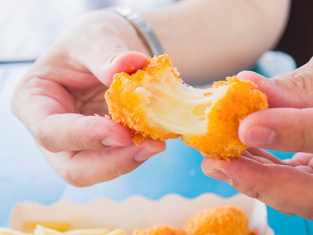 La mano è in possesso di una palla di formaggio stretch pronta per essere mangiata con patatine fritte morbide e concentrate