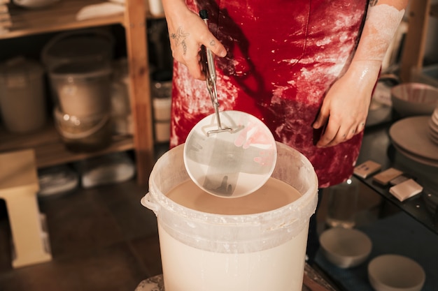 La mano femminile del vasaio che dipinge il piatto ceramico nell&#39;officina