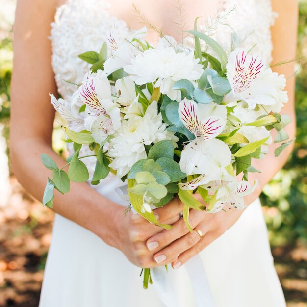 La metà di sezione delle mani di una sposa che tiene il bello mazzo del fiore