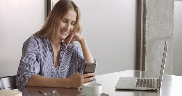 La modella bionda con una camicia abbottonata rilassata passa dal laptop al telefono al lavoro