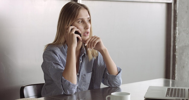 La modella bionda con una camicia abbottonata rilassata passa dal laptop al telefono al lavoro