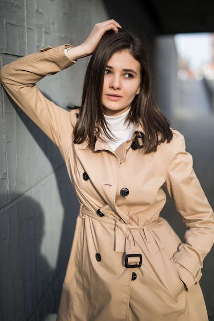 La modella bruna con gli occhi grandi rimane vicino alla parete grigia all'esterno