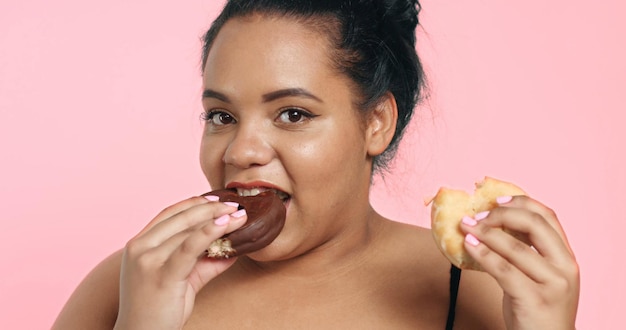 La modella plus size in studio spara sorridendo e mangia una ciambella