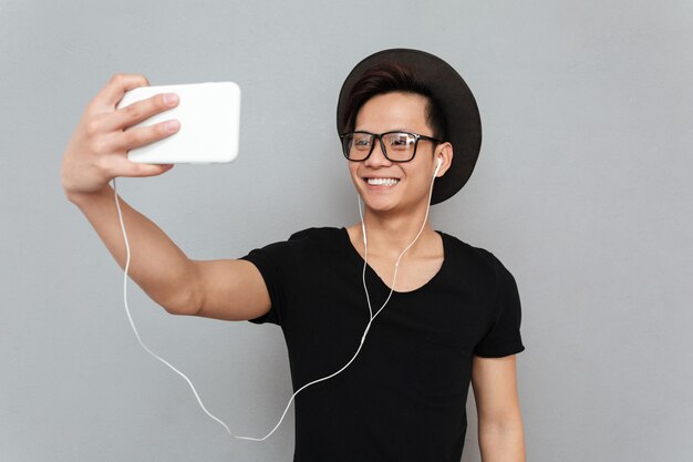 La musica d'ascolto sorridente del giovane uomo asiatico e fa il selfie