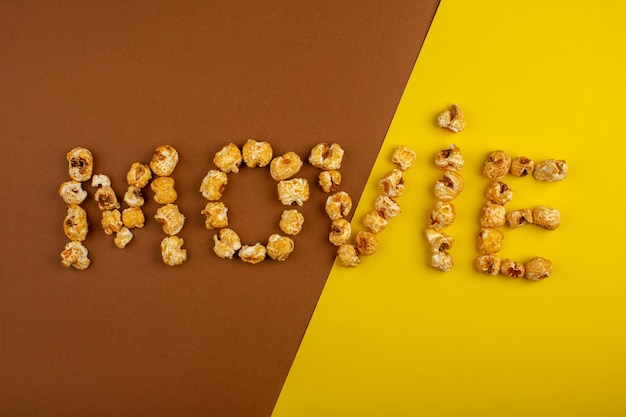 La parola film popcorn ha modellato con popcorn dolce su uno scrittorio giallo marrone