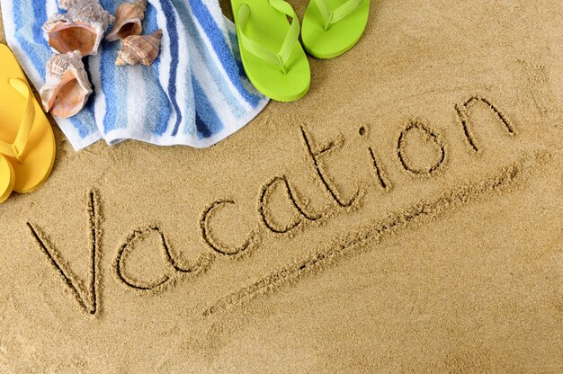 La parola vacanza scritta in sabbia con infradito e telo mare