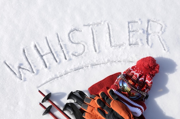 La parola Whistler scritto nella neve con bastoncini da sci, occhiali e cappelli