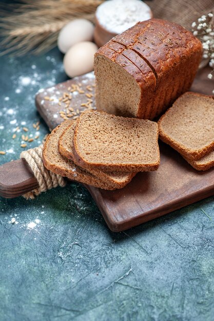 La parte superiore dei grani di pane nero dietetico su tavola di legno picchia la farina di uova di fiori in una ciotola su sfondo blu