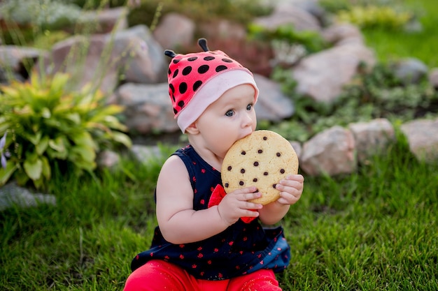 La piccola bambina con un grande biscotto al cioccolato si siede sul cortile