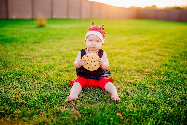 La piccola bambina con un grande biscotto al cioccolato si siede sul cortile