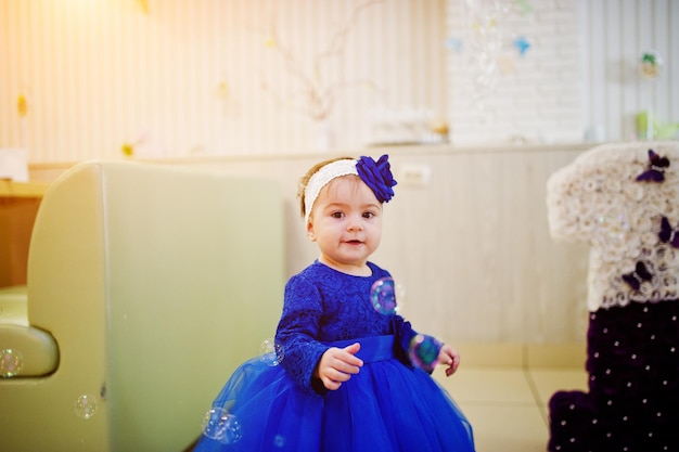 La piccola neonata sveglia al vestito blu gioca con le bolle di sapone il giorno di compleanno di 1 anno