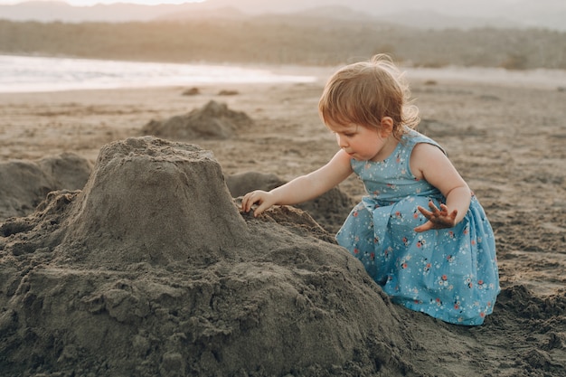 La piccola ragazza caucasica si diverte scavando nella sabbia alla spiaggia dell&#39;oceano, costruendo il castello della sabbia
