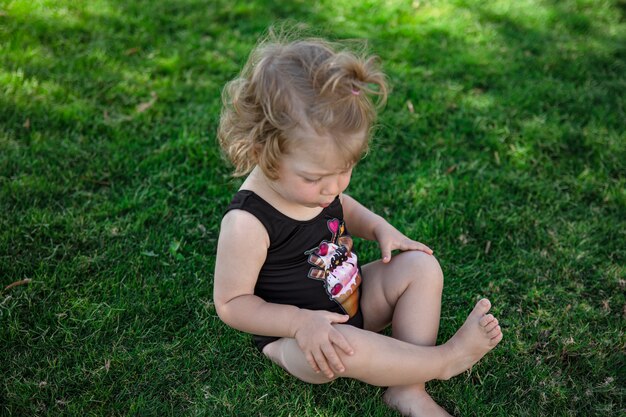 La piccola ragazza divertente in estate si siede sull'erba in giardino