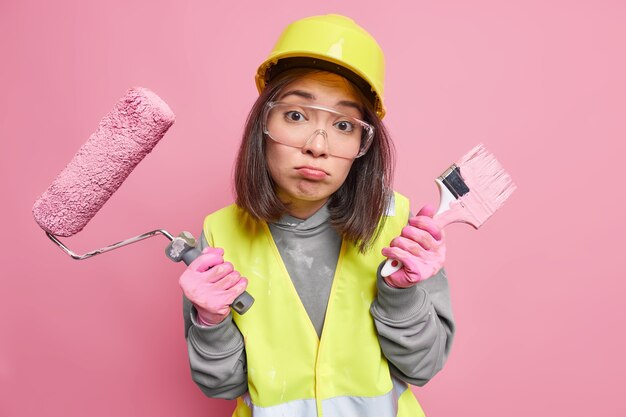 la pittrice sembra infelicemente increspa le labbra tiene il pennello e il rullo vestito in uniforme andando a ridecorare casa