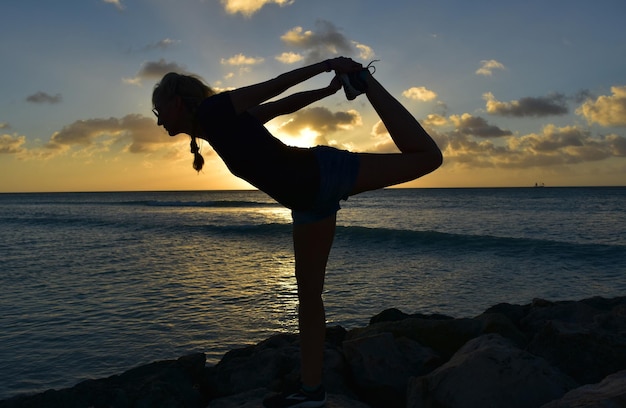 La posa del ballerino di yoga si staglia mentre il sole tramonta contro il cielo