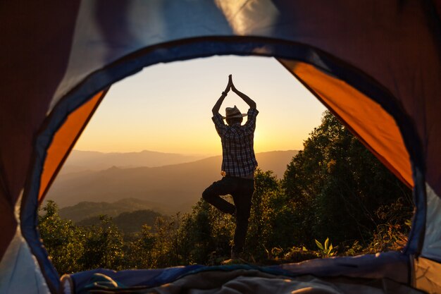 la posizione anteriore di posizione di yoga dell&#39;uomo della tenda di campeggio emette luce con l&#39;alba nella mattina