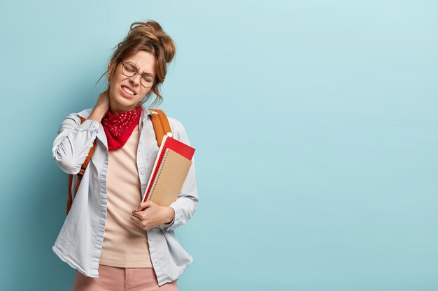 La pupilla o lo studente stanco inclina la testa sul lato destro, tocca il collo, soffre di dolore dopo un duro lavoro, stringe i denti