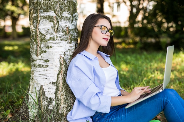 La ragazza abbastanza seria in blue jeans lavora con il computer portatile nel citypark