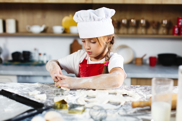 La ragazza affascinante si diverte a fare i biscotti di un impasto in una cucina accogliente