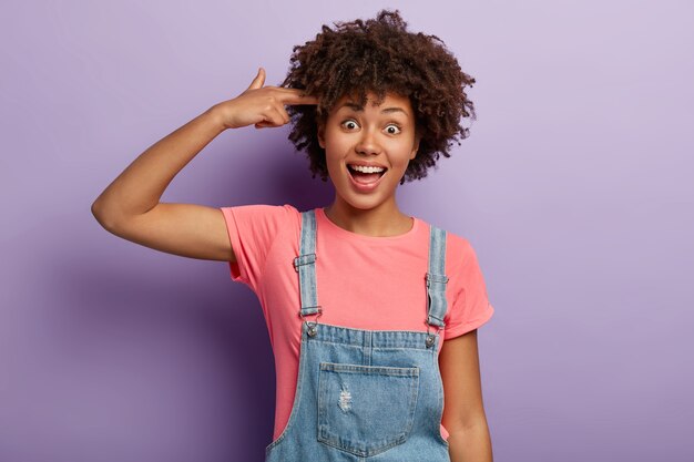 La ragazza afro positiva divertente fa il gesto della pistola, spara nella tempia, mostra il segno di suicidio