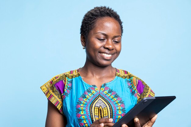 La ragazza afroamericana è felice di usare il tablet sullo sfondo blu