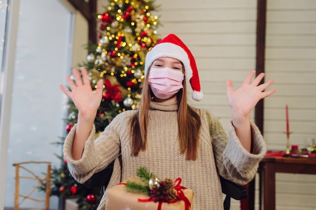 La ragazza agita la mano a Capodanno. Albero di Natale. Natale durante il coronavirus, concetto