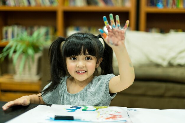 La ragazza allegra si diverte a dipingere a colori con idee creative presenti e mani disordinate a casa