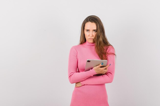 La ragazza arrabbiata sta alzando lo sguardo abbracciando il suo computer tablet su sfondo bianco