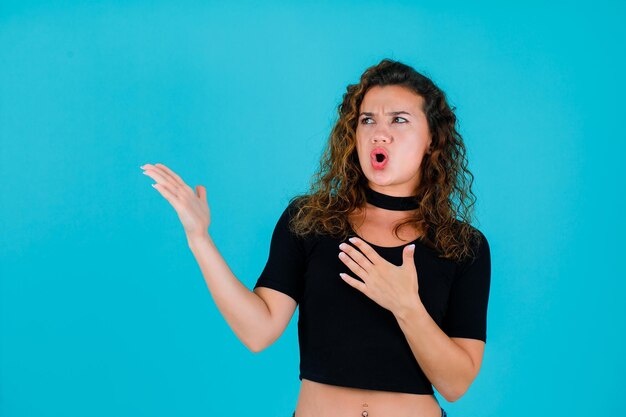 La ragazza arrabbiata sta guardando a sinistra indicando a sinistra con le mani su sfondo blu